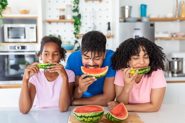Familie eet een zoete watermeloen in de keuken Een man en een vrouw met een dochter eten een rijpe watermelon in de keuken Een gelukkige familie die watermeroen eet