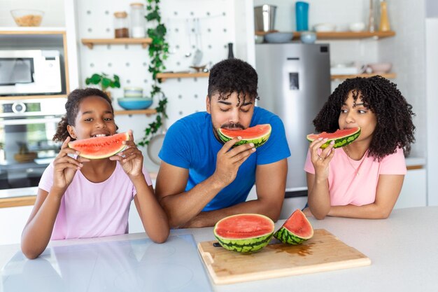 Familie eet een zoete watermeloen in de keuken Een man en een vrouw met een dochter eten een rijpe watermelon in de keuken Een gelukkige familie die watermeroen eet