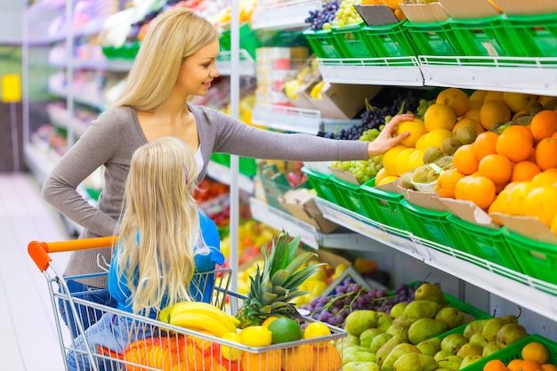 Familie eten winkelen. vrouw moeder en dochtertje kiezen fruit in de supermarkt