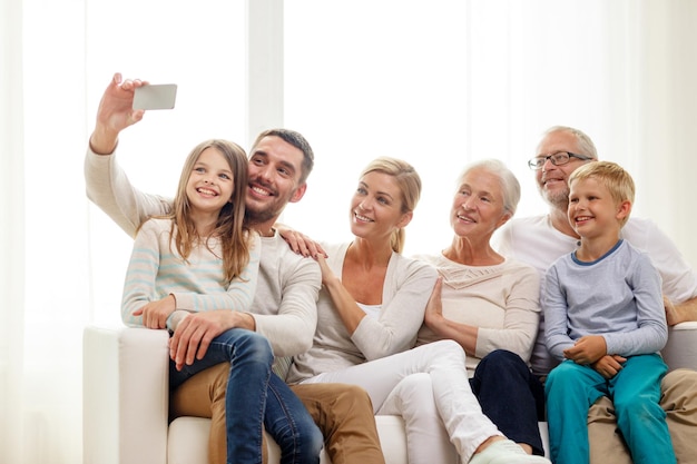 familie, geluk, generatie en mensen concept - gelukkige familie zittend op de bank en selfie maken met smartphone thuis