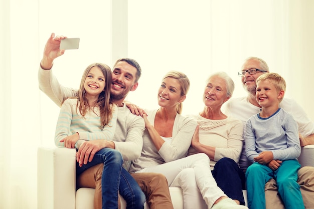 familie, geluk, generatie en mensen concept - gelukkige familie zittend op de bank en selfie maken met smartphone thuis