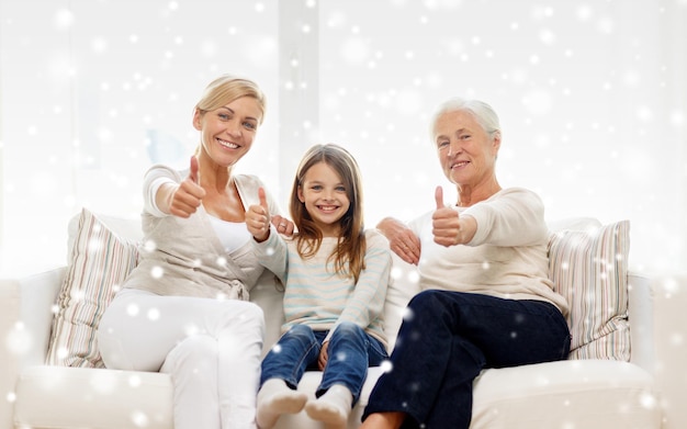 familie, geluk, generatie en mensen concept - glimlachende moeder, dochter en grootmoeder zittend op de bank en duimen omhoog gebaar thuis laten zien