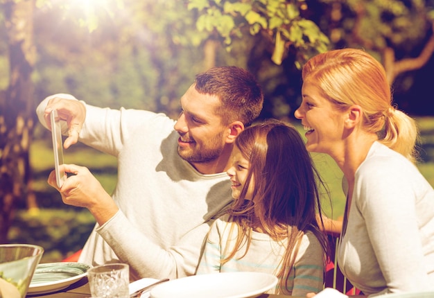 familie, geluk, generatie, huis en mensen concept - gelukkig gezin aan tafel zitten en selfie nemen met tablet pc-computer buitenshuis