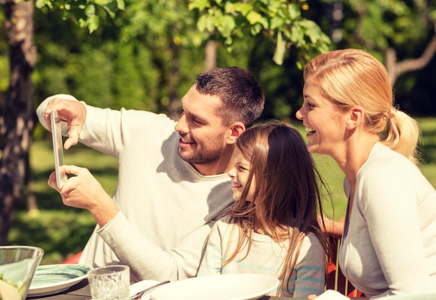 Foto familie, geluk, generatie, huis en mensen concept - gelukkig gezin aan tafel zitten en selfie nemen met tablet pc-computer buitenshuis