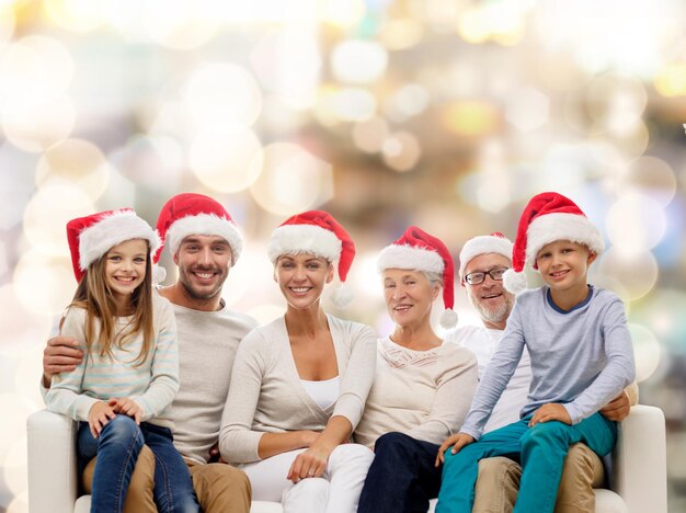 familie, geluk, generatie, vakantie en mensen concept - gelukkige familie in santa helper hoeden zittend op de bank over lichten achtergrond