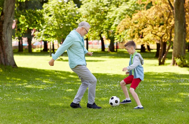 familie-, generatie-, spel-, sport- en mensenconcept - gelukkige grootvader en kleinzoon voetballen in het zomerpark