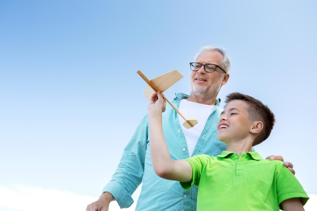 familie, generatie, toekomst, droom en mensenconcept - gelukkige grootvader en kleinzoon met speelgoedvliegtuig over blauwe hemel