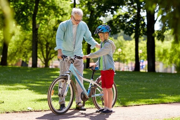 familie, generatie, veiligheid en mensenconcept - gelukkige grootvader die jongen onderwijst met fiets en fietshelm in het zomerpark