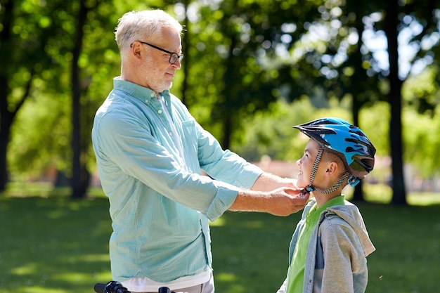 familie, generatie, veiligheid en mensenconcept - gelukkige grootvader helpt jongen met fietshelm in zomerpark