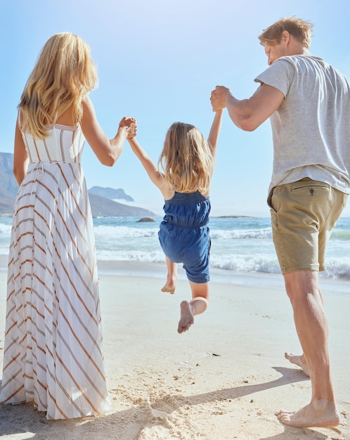 Familie genieten van een leuke dag op het strand en spelen met hun kleine meisje Achteraanzicht van een blonde moeder en vader die hun schattige dochtertje in de lucht zwaaien op het strand op een zonnige zomerdag