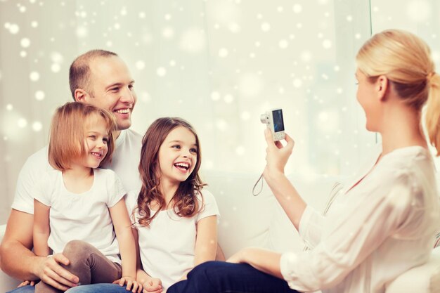 Foto familie, huis, technologie en mensen - gelukkig gezin met camera die foto maakt over sneeuwvlokkenachtergrond