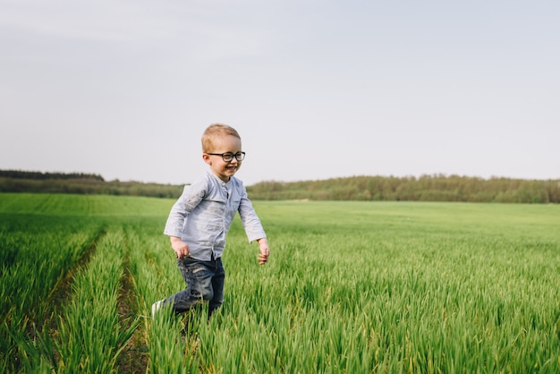 Familie in de natuur. Picknick in het bos, in de weide. Blauwe kleding. De jongen in glazen met blond haar. Vreugde. Loopt door het groene gras.