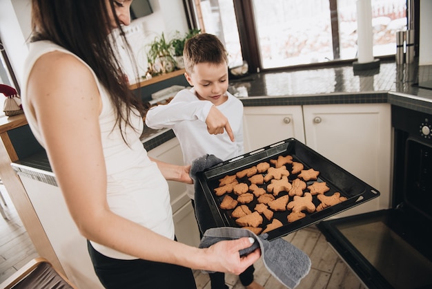 Familie in een groot huis. Lifestyle Thuiscomfort. Kinderen thuis. Bak peperkoekkoekjes met mama. Klaar hete koekjes. Mooie keuken.