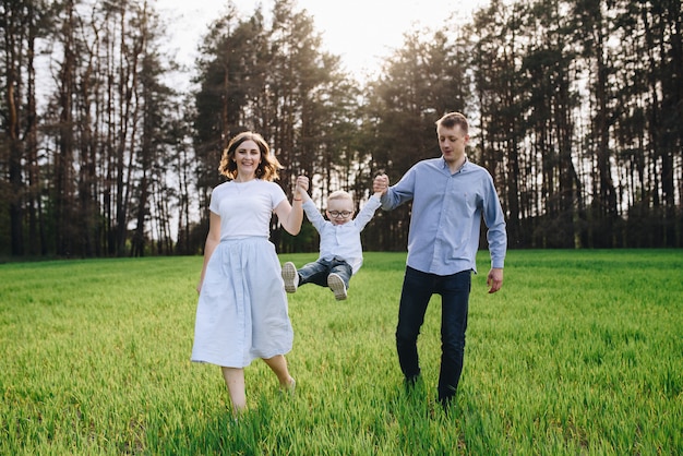 Familie in het bos op een picknick. Ga op een open, groen gras zitten. Blauwe kleding. Mam en pap spelen met hun zoon, knuffelen en glimlachen. Een kind met een bril. Tijd samen