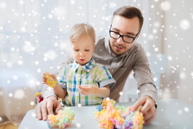 familie, jeugd, creativiteit, activiteit en mensenconcept - gelukkige vader en zoontje spelen thuis met balklei over sneeuw