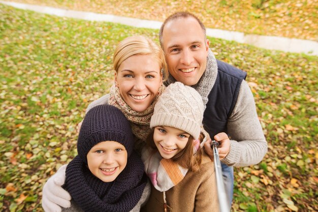 familie, jeugd, seizoen, technologie en mensenconcept - gelukkig gezin fotograferen met selfiestick in herfstpark