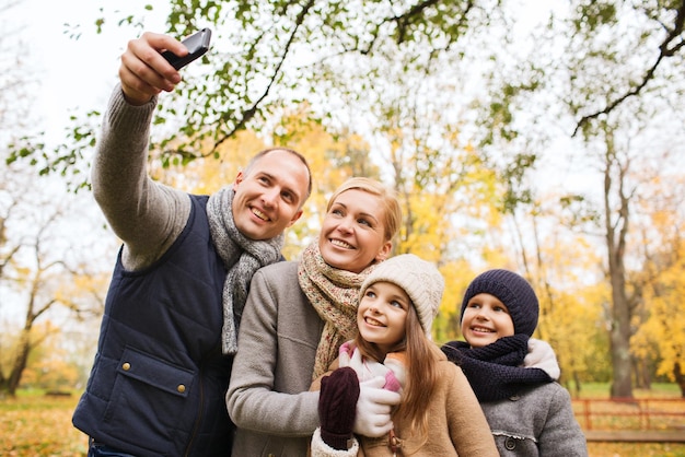 familie, jeugd, seizoen, technologie en mensenconcept - gelukkige familie die selfie neemt met smartphone in herfstpark