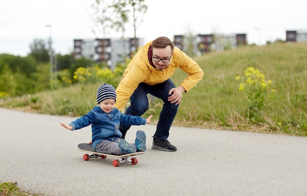 familie, jeugd, vaderschap, vrije tijd en mensenconcept - gelukkige vader en zoontje rijden op skateboard