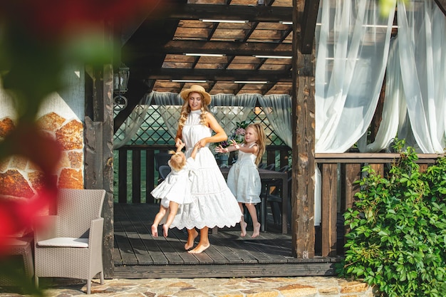 Foto familie jonge volwassen mooie vrouw moeder in een jurk met kinderen op het terras bij house