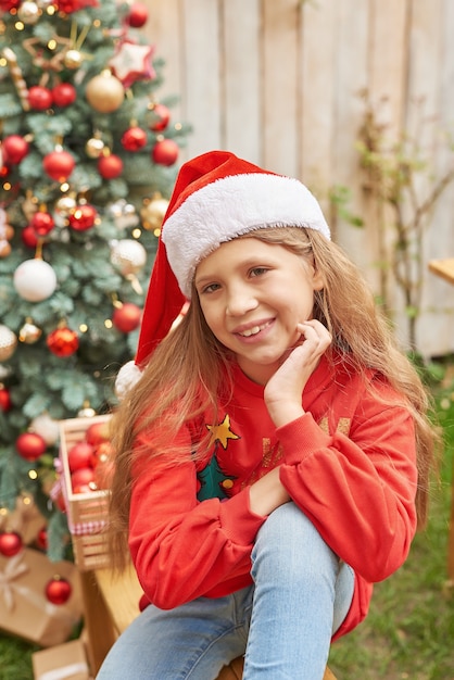 Familie kerst in juli. portret van meisje in de buurt van kerstboom met geschenken. baby decoreren grenen. wintervakantie en mensen concept. prettige kerstdagen en gelukkig vakantie wenskaart. kerst kind