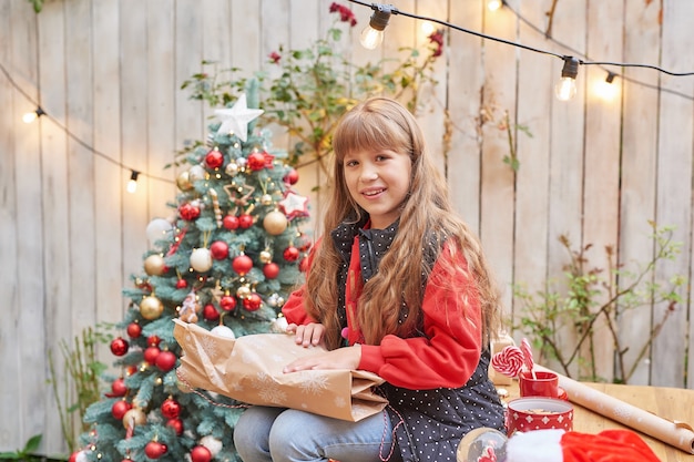 Familie kerst in juli. Portret van meisje in de buurt van kerstboom met geschenken. Baby decoreren grenen. Wintervakantie en mensen concept. Prettige kerstdagen en gelukkig vakantie wenskaart. kerst kind