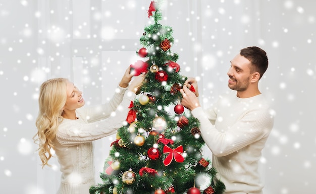 Familie, Kerstmis, de wintervakantie en mensenconcept - gelukkig paar die Kerstmisboom thuis verfraaien