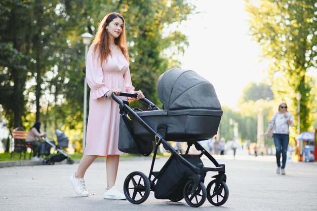 Familie, kind en ouderschap concept - gelukkige moeder wandelen met kinderwagen in park.