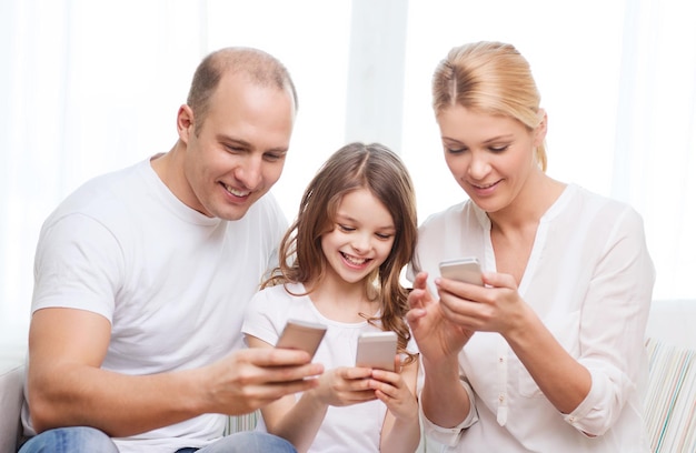 familie, kind, technologie en thuisconcept - lachende ouders en klein meisje met smartphones thuis