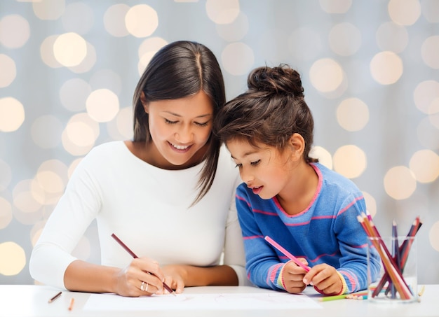 familie, kinderen, creativiteit en gelukkige mensen concept - gelukkige moeder en dochter tekenen met potloden over vakantie lichten achtergrond