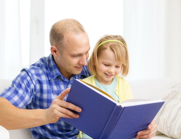 familie, kinderen, onderwijs, school en gelukkige mensen concept - glimlachende vader en dochter met boek thuis