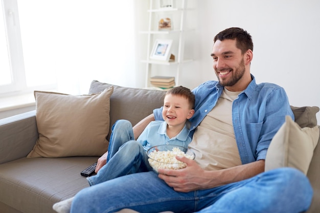 familie, kindertijd, vaderschap, technologie en mensen concept - gelukkige vader en kleine zoon met afstandsbediening en popcorn thuis tv kijken