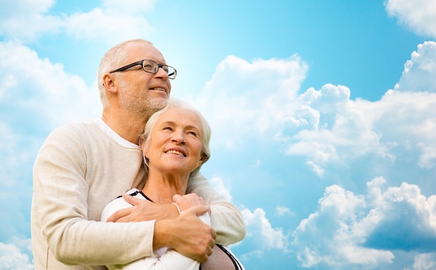 familie, leeftijd, liefde, relaties en mensen concept - gelukkig senior paar knuffelen over blauwe lucht en wolken achtergrond