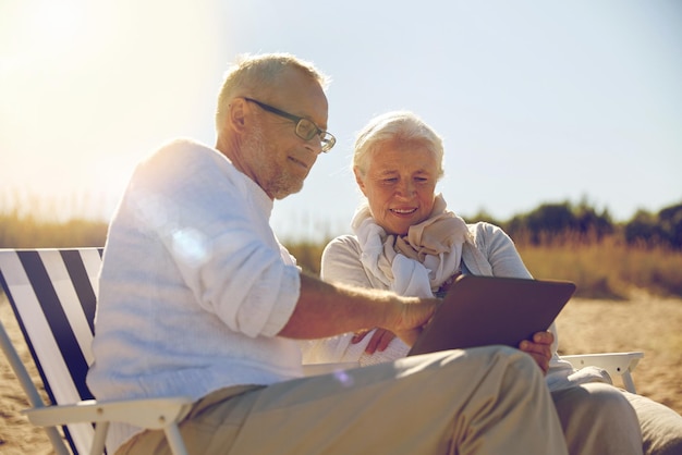 familie, leeftijd, reizen, toerisme en mensen concept - gelukkig senior paar met tablet pc-computer rusten in klapstoelen op zomerstrand