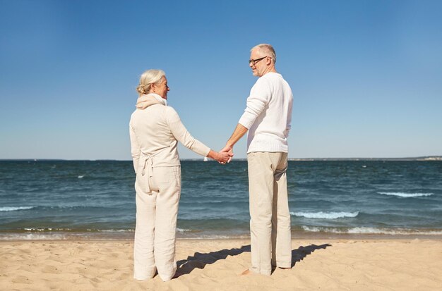 familie, leeftijd, reizen, toerisme en mensenconcept - gelukkig senior paar hand in hand op zomerstrand