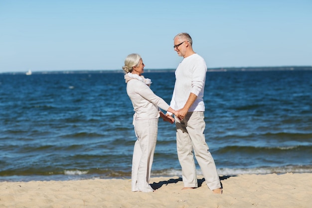 familie, leeftijd, reizen, toerisme en mensenconcept - gelukkig senior paar hand in hand op zomerstrand