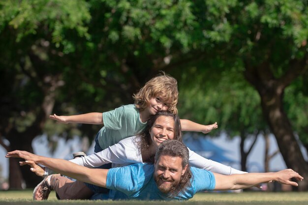 Familie liggend op gras in park ouders geven kind meeliften in platteland vliegen concept kleine jongen...