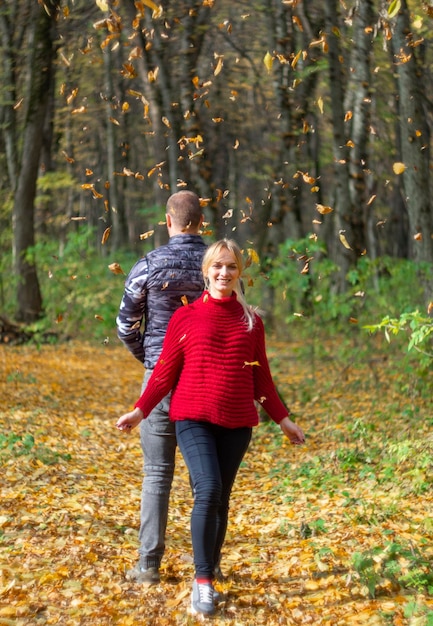 Familie man en zwangere vrouw in een rode trui tussen de gevallen bladeren in het herfstbos