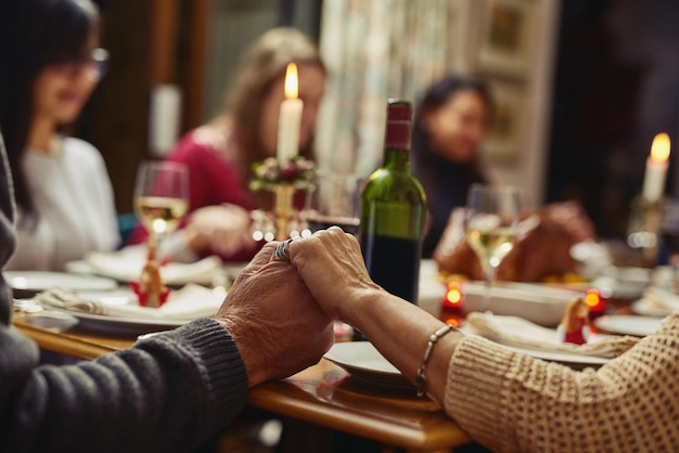 Foto familie mensen hand in hand in gebed en aan tafel met champagne bidden voor voedselondersteuning of liefde en volwassenen komen samen voor een feest of dankzegging in de eetkamer bij hen thuis