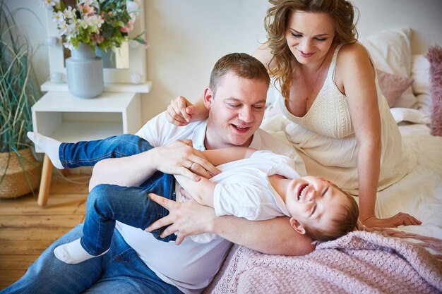 Familie met een klein kind heeft plezier thuis in de buurt van het bed.