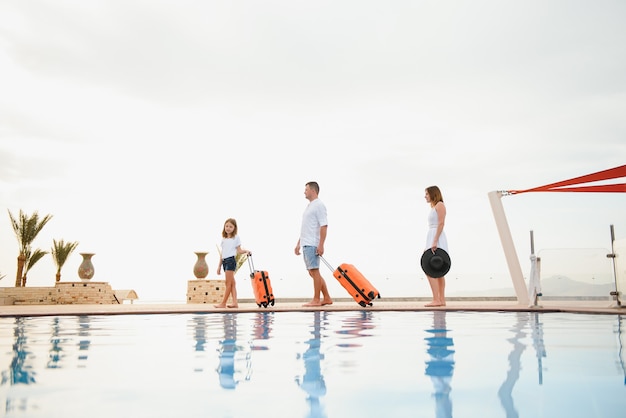 familie met koffers lopen naar hotelgebouw met prachtig zwembad. reizend concept.