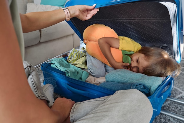 Familie moeder en kind hebben plezier, het kind verstopt zich in een koffer en pakt dingen en reiskussen in voor een reis
