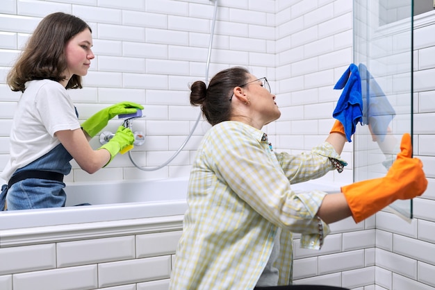 Familie moeder en tienerdochter die samen thuis in de badkamer schoonmaken. Kind helpt ouder, huishouden, levensstijl, huishoudelijk werk