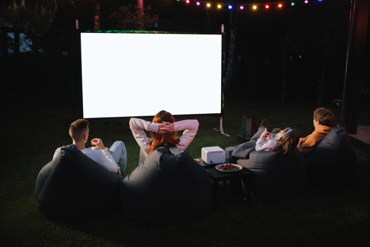 Familie moeder vader en kinderen kijken 's avonds op de binnenplaats naar een projectorfilms met popcorn