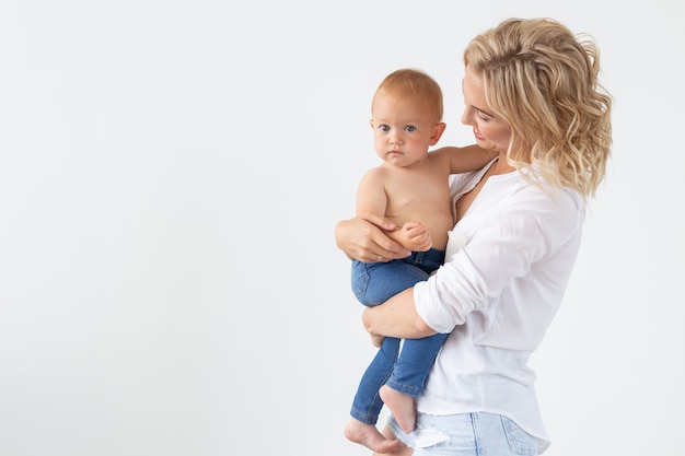 Familie, moederschap en familieconcept - Jonge moeder die haar baby op witte muur houdt