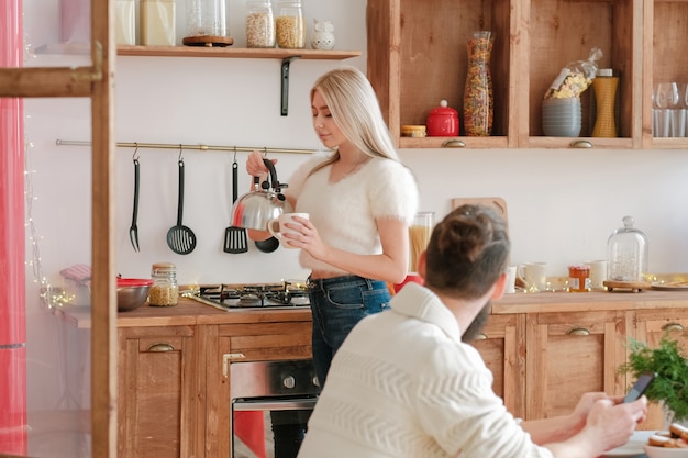 Familie ochtend. Mooie blonde dame die thee voor haar echtgenoot in moderne keuken maakt.