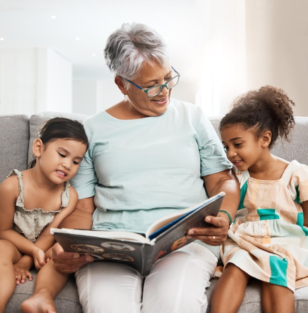 Familie oma en kinderen met boeklezing op de bank voor hechting, ontspanning en quality time samen Liefdesonderwijs en oudere vrouw met meisjes leren verhaal, sprookje en literatuur te lezen