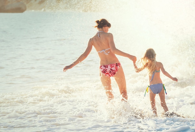 Familie op het strand bij zonsondergang. Moeder en dochter lopen samen.