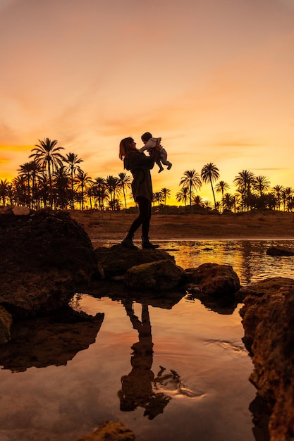 Familie op het strand jonge moeder met haar baby aan zee bij oranje zonsondergang