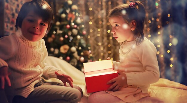 Familie op kerstavond bij open haard. Kinderen openen kerstcadeautjes. Kinderen onder de kerstboom met geschenkdozen. Ingerichte woonkamer met traditionele open haard. Gezellige warme winteravond in huis.