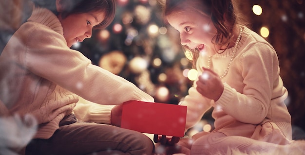 Familie op kerstavond bij open haard. Kinderen openen kerstcadeautjes. Kinderen onder de kerstboom met geschenkdozen. Ingerichte woonkamer met traditionele open haard. Gezellige warme winteravond in huis.